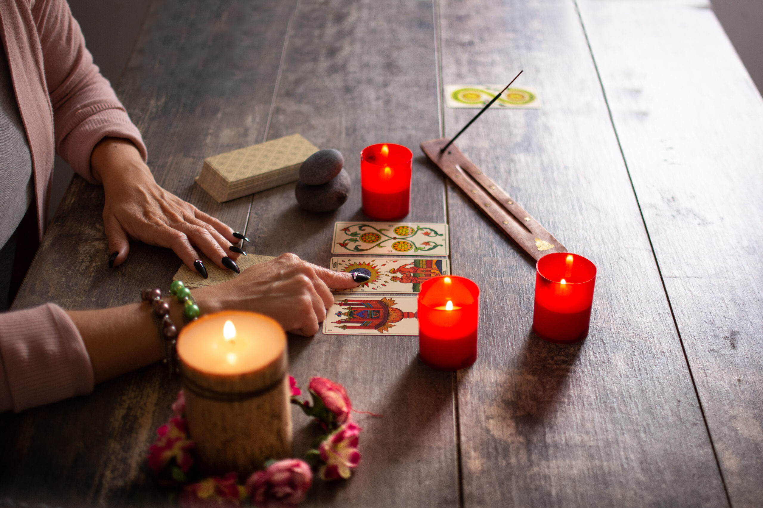 Em uma mesa, aparece mãos de uma mulher tirando cartas de tarot do lado de velas